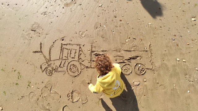 Enfant dessinant un tracteur d'ostréiculteur et sa remorque sur du sable mouillé