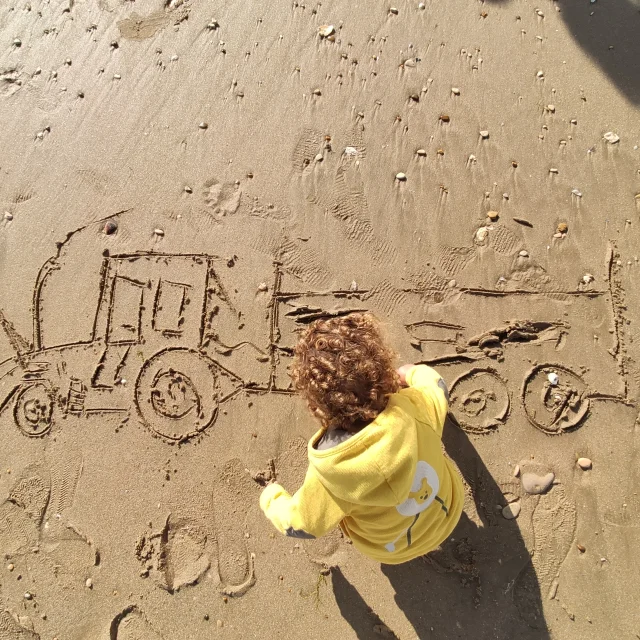 Enfant dessinant un tracteur d'ostréiculteur et sa remorque sur du sable mouillé