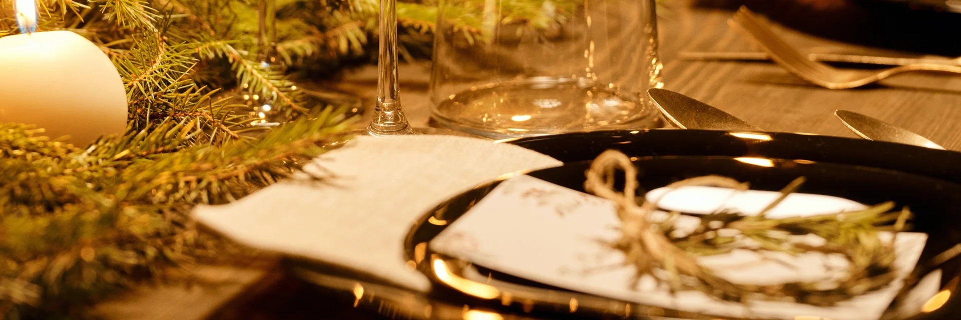 Table dressée pour un dîner festif, décorée de bougies, de verres à vin et de branches de sapin.