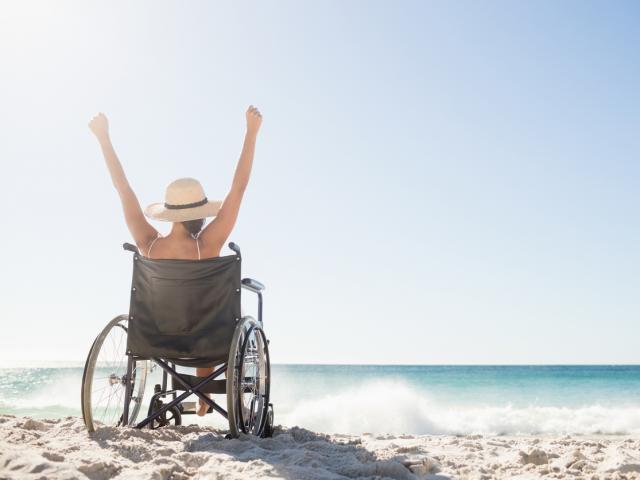 Wheelchair woman sitting  with arms up on the beach