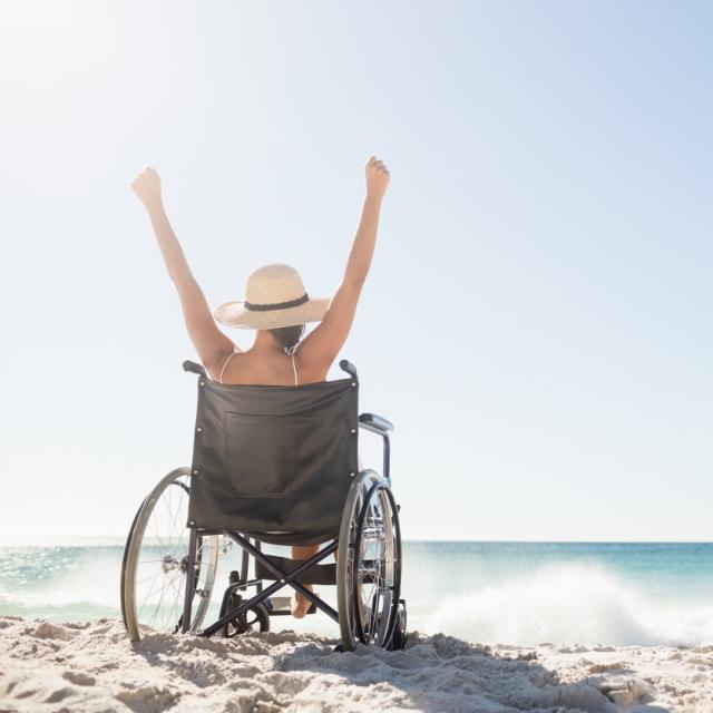 Wheelchair woman sitting  with arms up on the beach