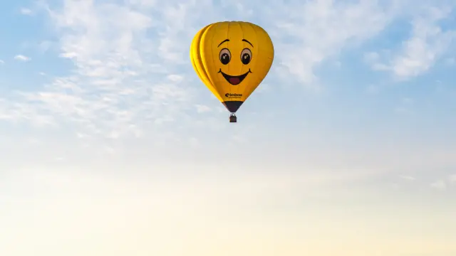 Une montgolfière jaune avec un visage de smiley volant au-dessus d'un paysage montagneux.