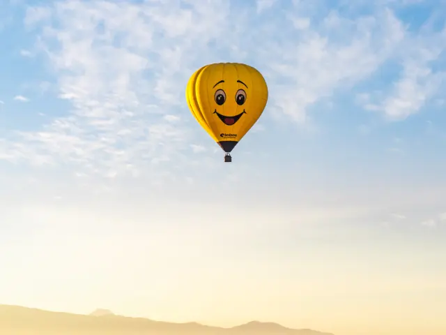 Une montgolfière jaune avec un visage de smiley volant au-dessus d'un paysage montagneux.