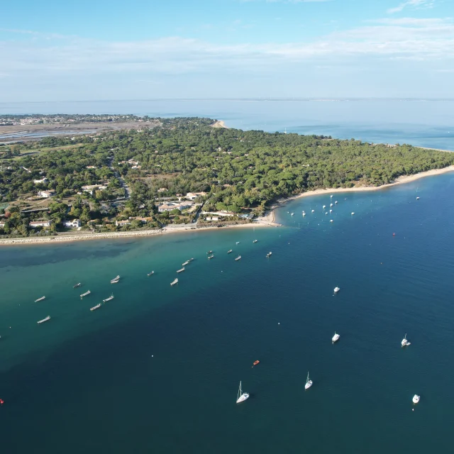 Vue aérienne d'une plage aux eaux turquoises avec quelques petits bateaux et la forêt derrière
