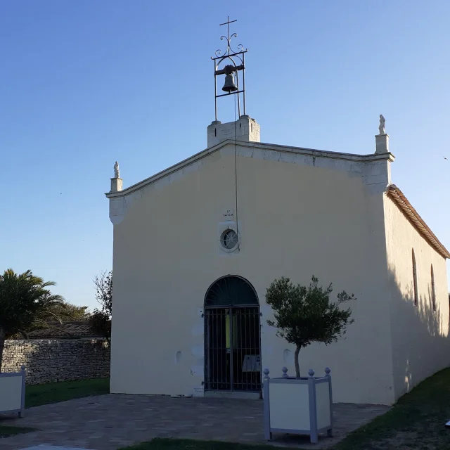 Chapelle avec une cloche au sommet et un arbre en pot devant au petit matin