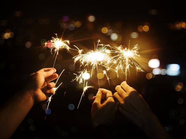 Mains tenant des cierges magiques allumés dans la nuit.