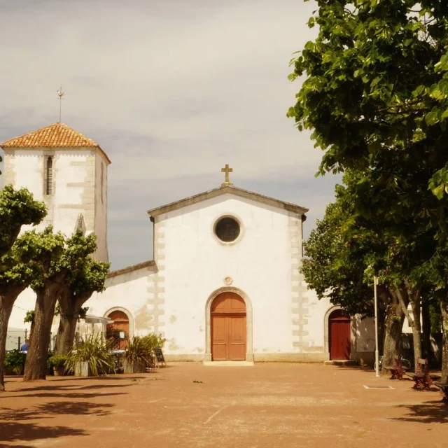 Place arborée de l'église de Loix avec l'édifice à la façade blanche en fond sous un ciel nuageux