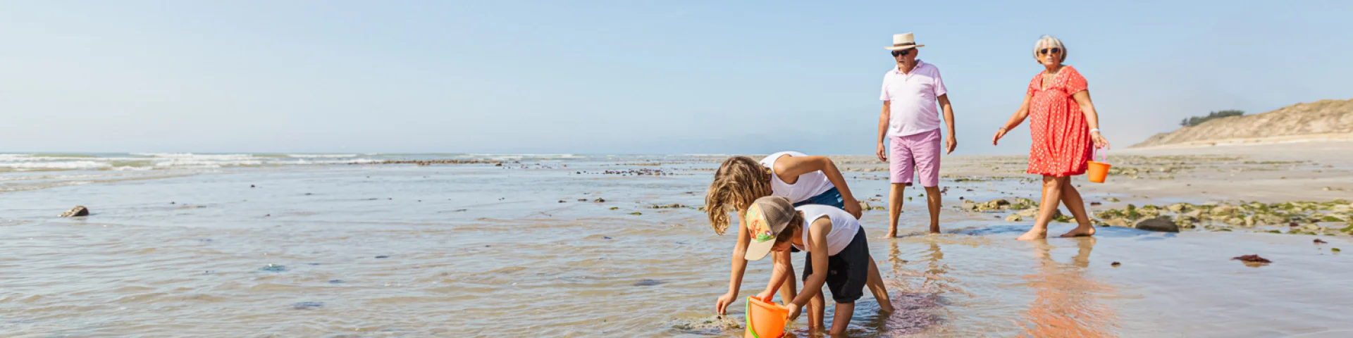 Famille pêchant à pied sur la plage à marée basse, cherchant des coquillages.