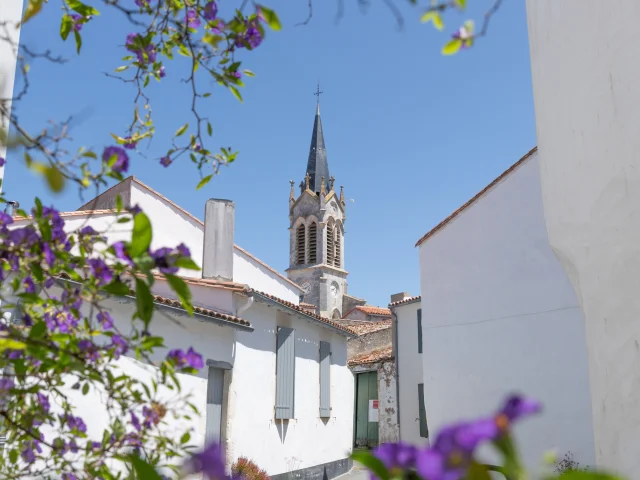 Clocher de l'église vu depuis une rue de La Couarde-sur-Mer avec des fleurs au premier plan.