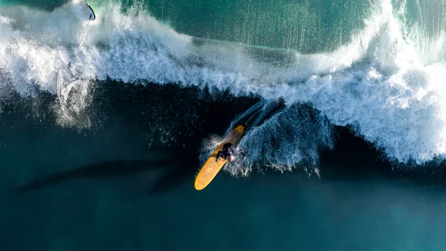 Surfeur capturé en action sur une grande vague vue de haut.