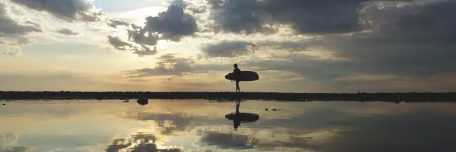 Surfeur marchant sur la plage au coucher de soleil