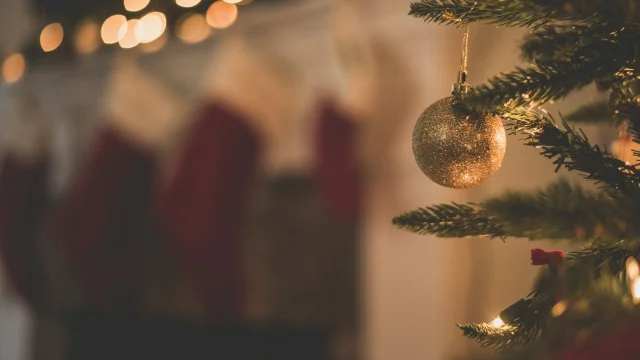 Boule dorée accrochée à un sapin de Noël illuminé avec des guirlandes.