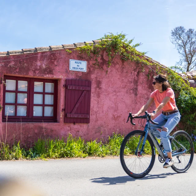Femme à vélo passant devant la maison rose des Portes-en-Ré.