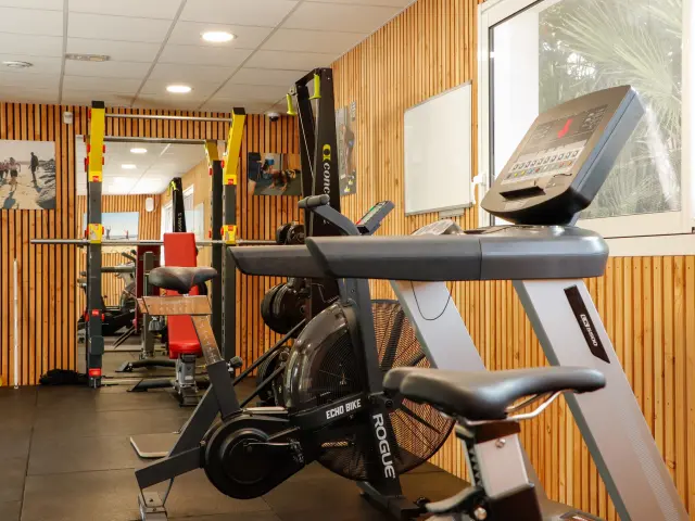 Salle de sport du Camping et Spa L’Océan avec équipements de fitness variés, ambiance boisée et éclairage naturel.