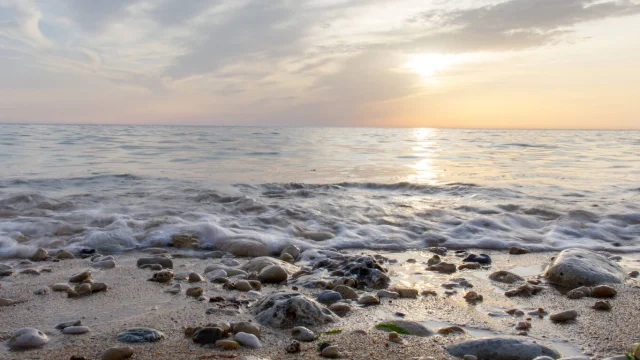 Plage avec des galets et des vagues sous un ciel au coucher du soleil.