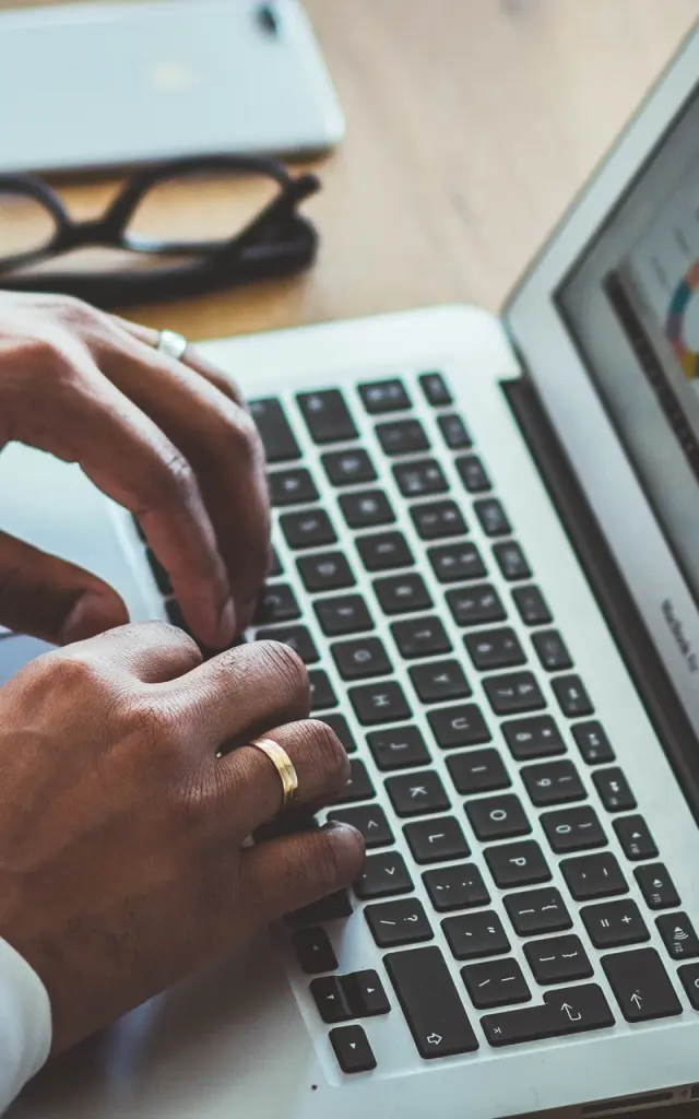Gros plan de mains d'un homme tapant sur le clavier d'un ordinateur portable affichant des graphiques de données colorés sur un bureau en bois.