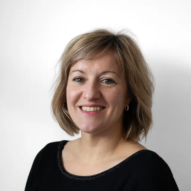 Portrait professionnel de Camille Pinot, une femme souriante aux cheveux châtains clairs mi-longs, portant un vêtement noir, sur un fond blanc neutre.