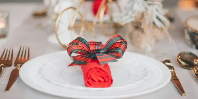 Assiette blanche ornée d’une serviette rouge roulée et nouée avec un ruban à carreaux rouges et verts.
