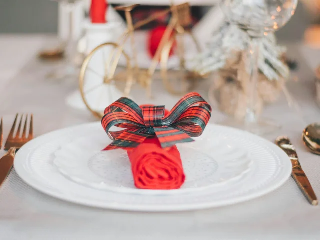 Assiette blanche ornée d’une serviette rouge roulée et nouée avec un ruban à carreaux rouges et verts.