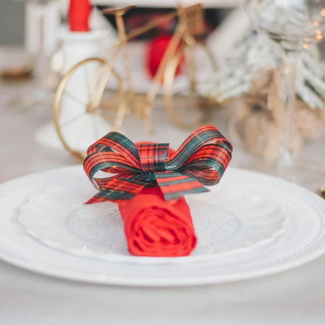Assiette blanche ornée d’une serviette rouge roulée et nouée avec un ruban à carreaux rouges et verts.