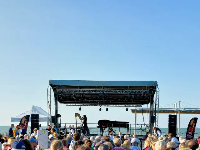 Photo d’un concert en bord de mer à Rivedoux-Plage, avec scène équipée d’un piano et d’une harpe, musiciens en représentation et public assis sous un ciel dégagé