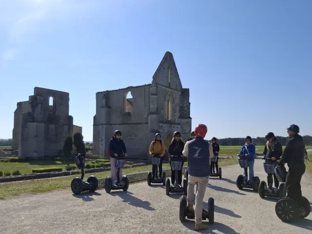 Un groupe de sept personnes à gyropode (Segway) encadré par un guide, devant les ruines de l'abbaye des Châteliers sur l'Île de Ré, par une journée ensoleillée.
