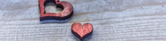 Two decorative red wooden hearts placed on a grey surface.