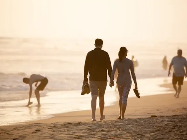 Several people are walking barefoot along a beach by the sea.