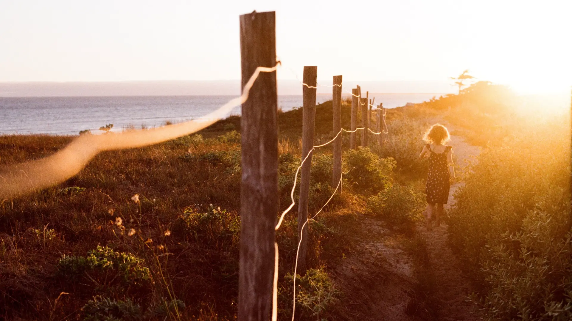 Enfant marchant sur un sentier bordé de piquets près de la mer au coucher du soleil