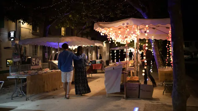 Allée de marché nocturne décorée de guirlandes lumineuses et bordée de stands.