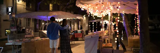 Allée de marché nocturne décorée de guirlandes lumineuses et bordée de stands.