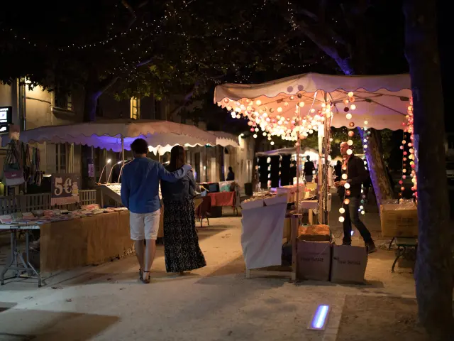 Allée de marché nocturne décorée de guirlandes lumineuses et bordée de stands.