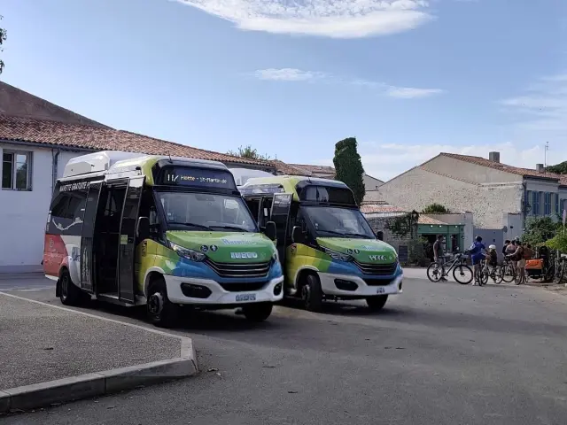 Deux navettes gratuites stationnées dans un village avec un parking à vélos à proximité.
